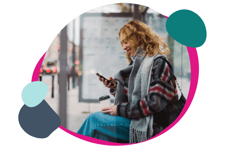 woman sat at a bus stop using her iPhone