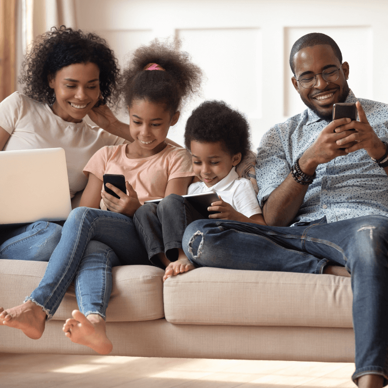 Family sat on the sofa using laptops and mobile