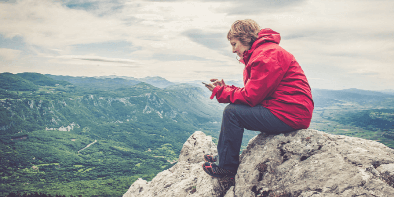 Woman sat on stones looking at smartphone