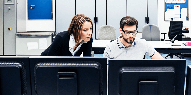 Two people looking at a desktop computer in an office